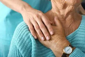 photo of an elderly woman being comforted by another person, their hand on top of hers