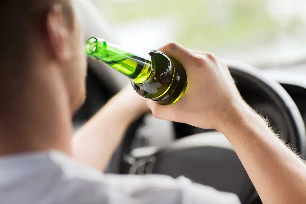 Photo of a man behind the wheel of a car, drinking a beer